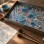 AI-generated illustration of blue and terracotta ebru patterns in a marbling tray beside a finished sheet, brushes, and pigment bowls.